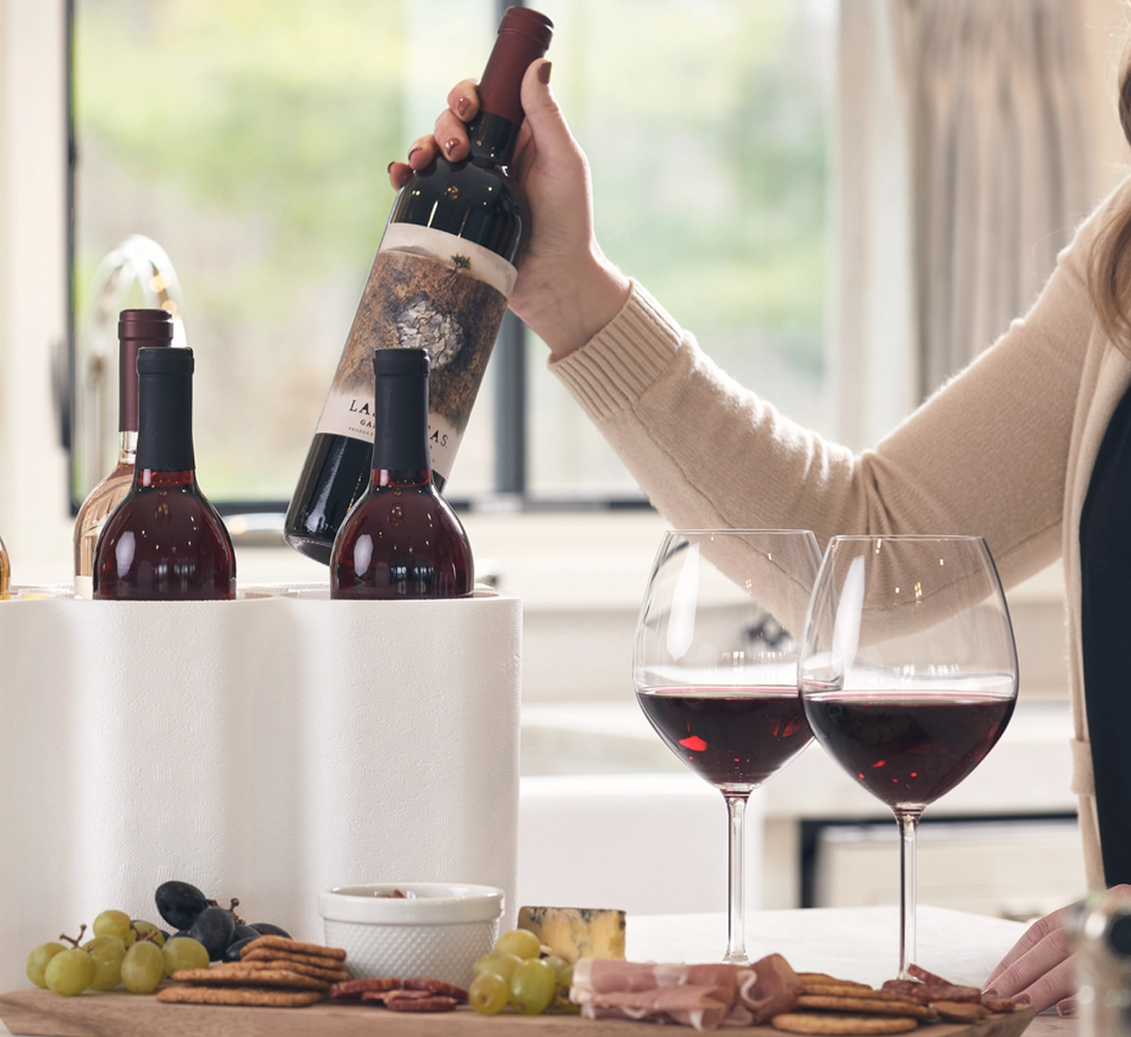 A woman lifting a bottle of wine from EPS foam packaging, next to a board of cheese and crackers.
