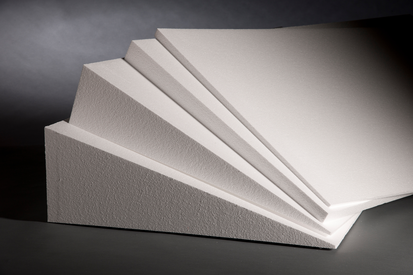 A stack of four EPS rigid insulation boards. They are all shaped in wedges of varying thickness. The thickest board is on the bottom and the thinnest board is on the top.